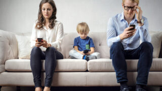 Young family is sitting on the couch and using mobile phones